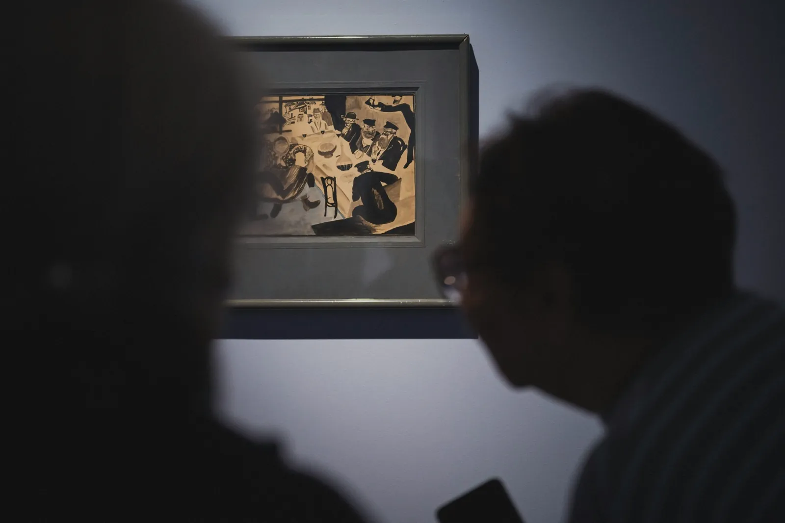 Two visitors in silhouette before a framed work on paper