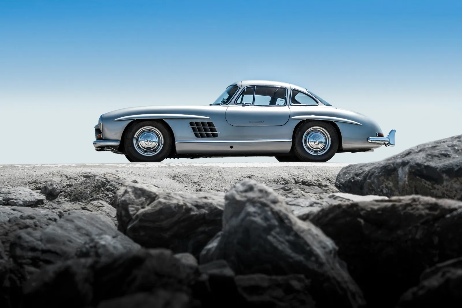 A silver Mercedes-Benz 300 SL Gullwing on a rocky shore